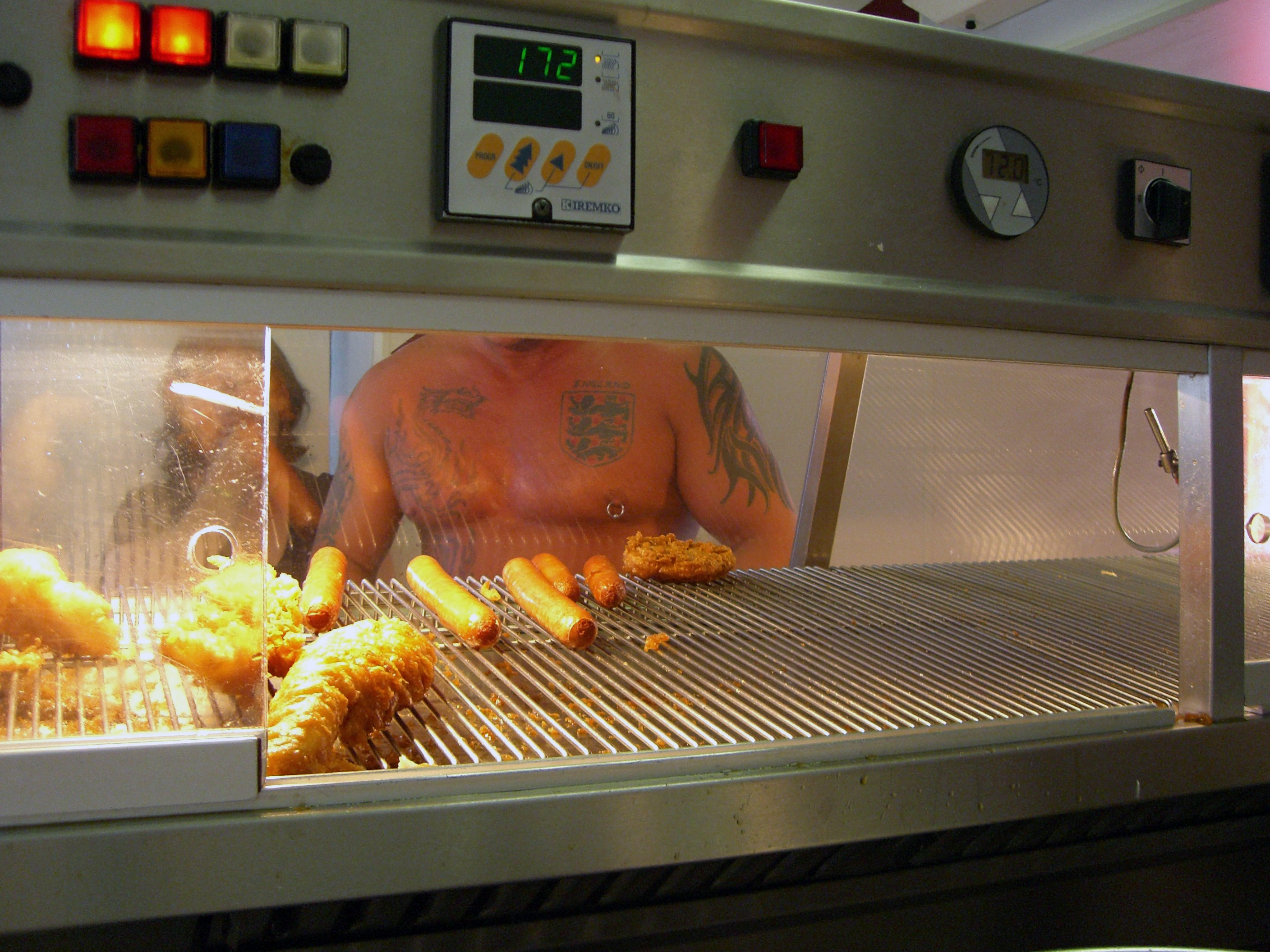 Male tattooed torso as viewed through a fish and chip shop heated counter. Photograph included in the exhibition Fried: Blackpool’s Fish And Chip Shops.