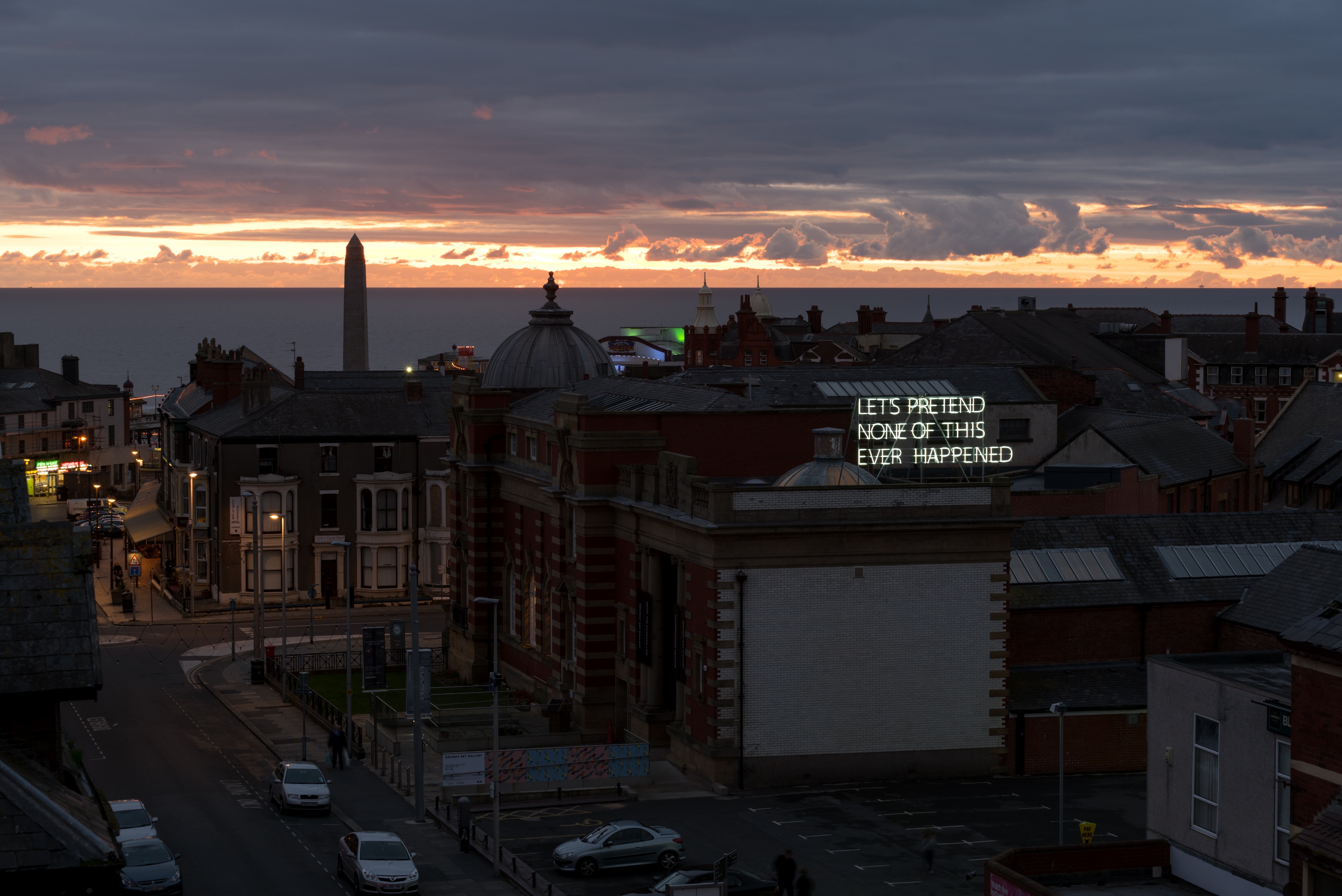 Side of The Grundy Art Gallery in the evening showing large neon artwork by artist Tim Etchells on roof as part of the 2016 Lightpool Festival. The neon says Let's Pretend None Of This Ever Happened.